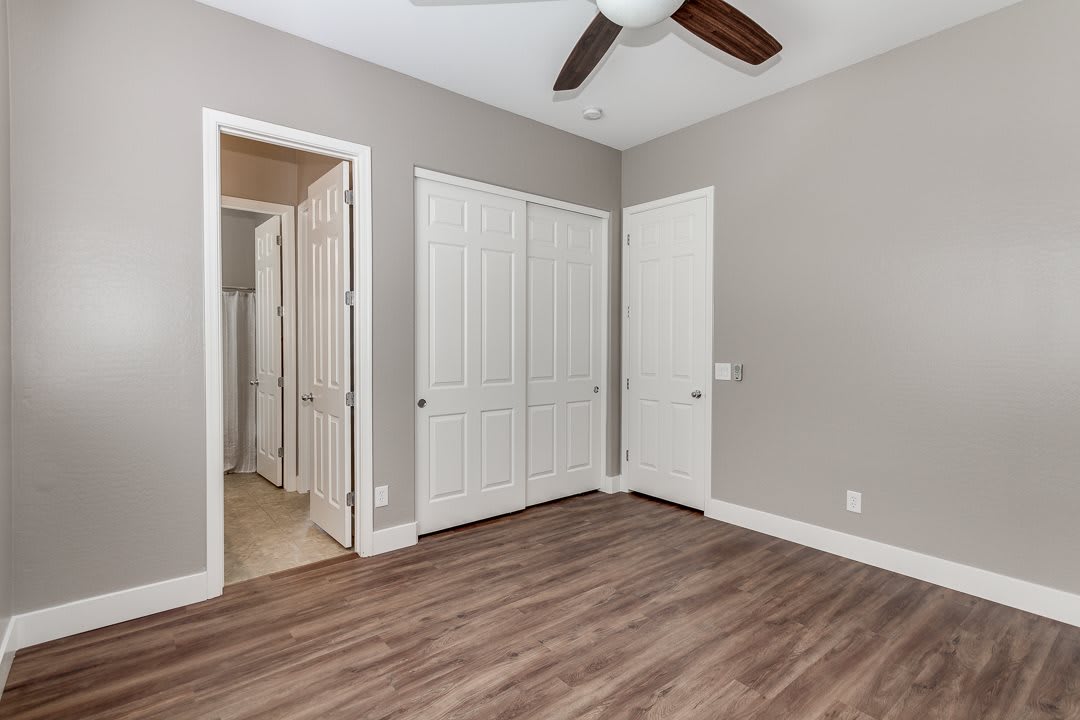 An empty room with a wooden floor, featuring a closet and ceiling fan.
