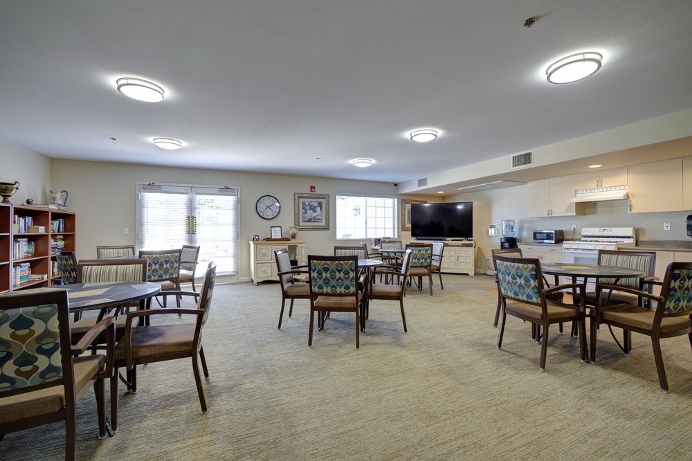A spacious and well-lit dining room with multiple tables and chairs, featuring a television on the wall.