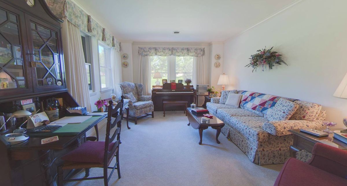 A bright and cozy living room with a sofa, armchairs, and a piano.