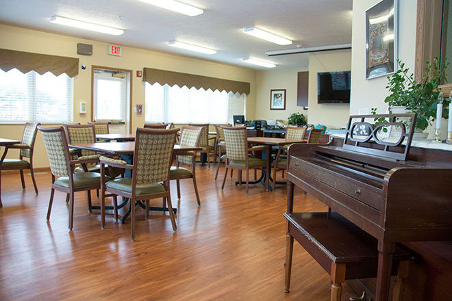 A community space with multiple tables and chairs, featuring a piano in the corner.