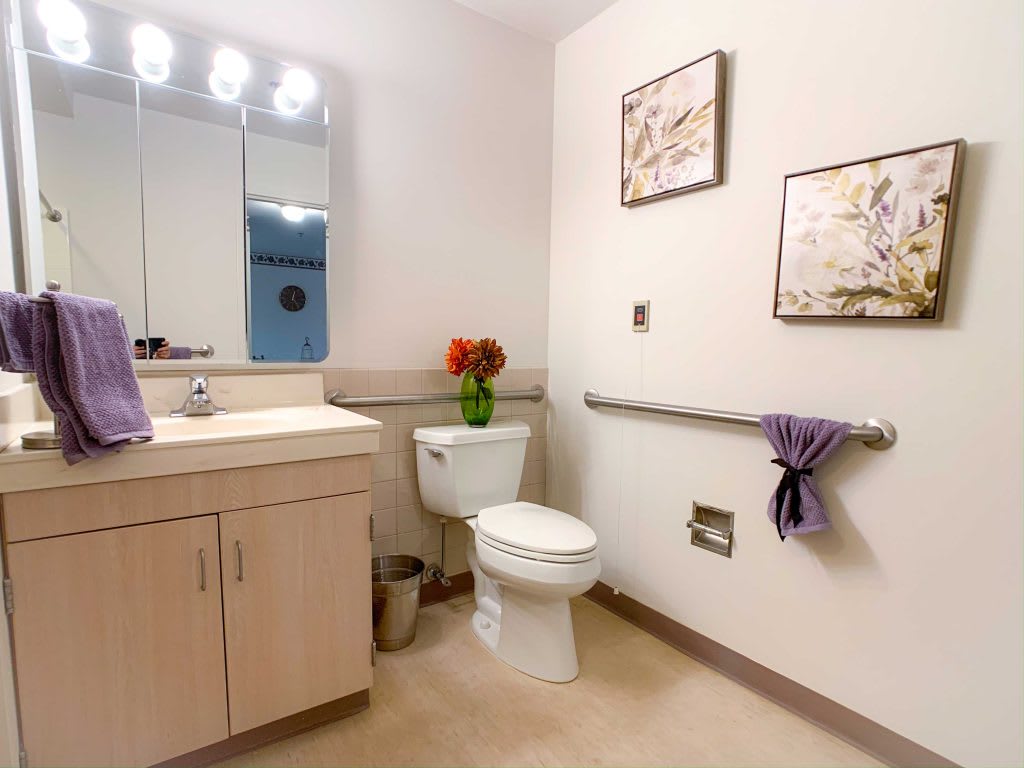 A clean and modern bathroom featuring a toilet, sink, mirror, and decorative elements such as flowers and artwork.