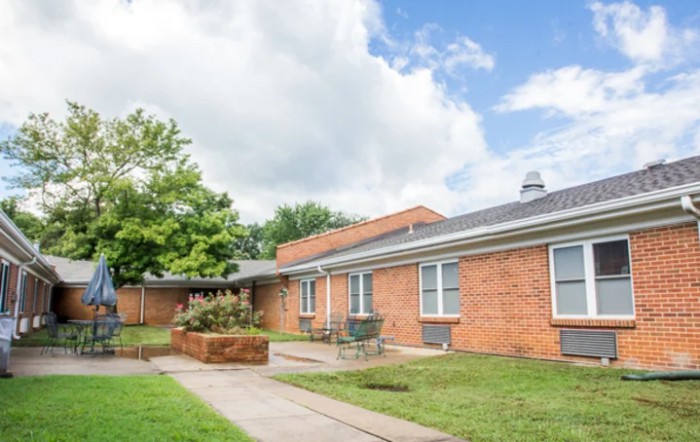 A single-story brick residential building with a yard and cloudy sky.