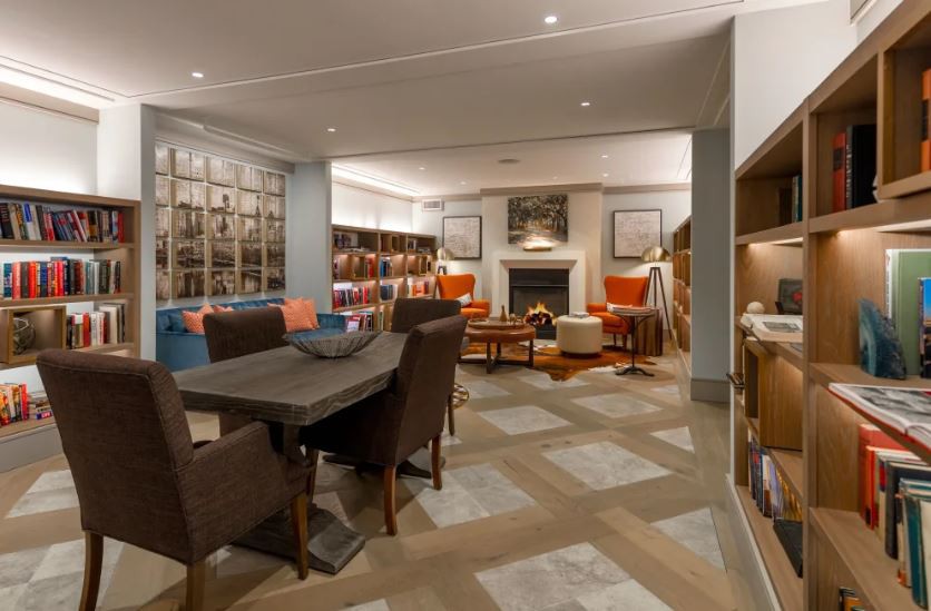 A cozy library interior with bookshelves and comfortable seating around a fireplace.