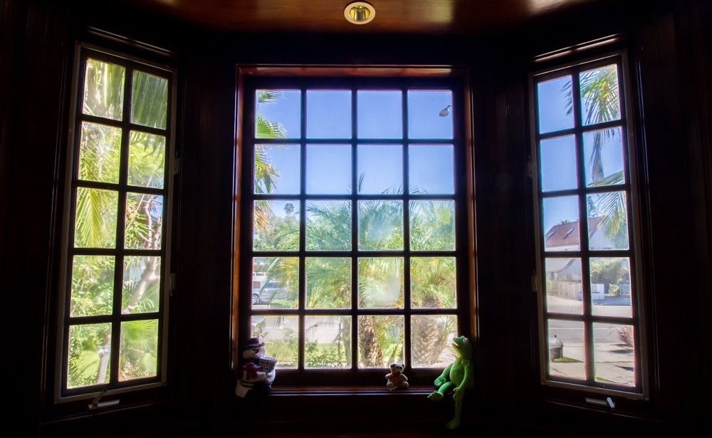 A view through a large window with palm trees outside, accompanied by toys on the windowsill.