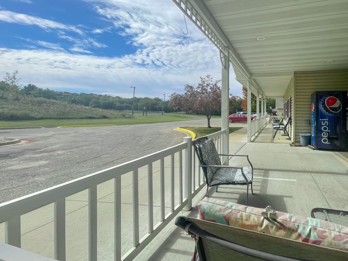 A sunny day on a porch overlooking an open parking lot and green landscape.