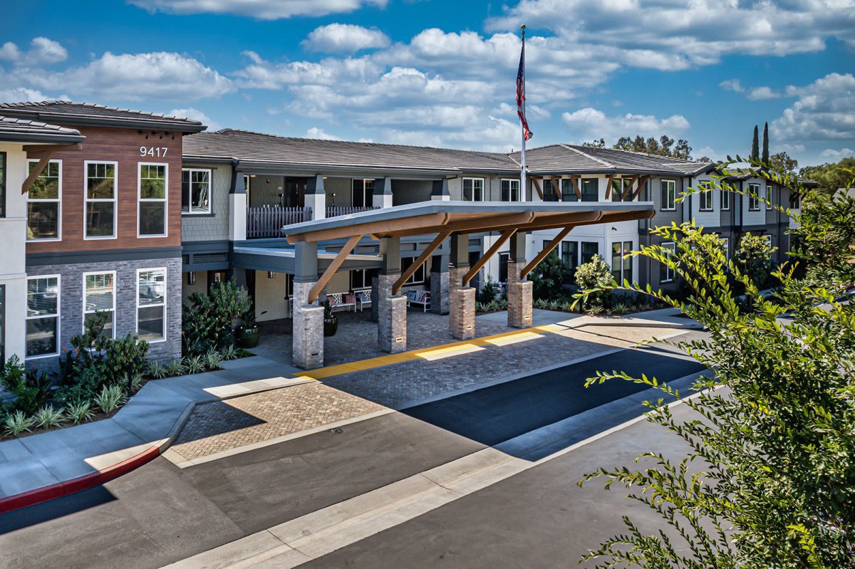 An exterior view of a modern building entrance with a covered walkway and a clear blue sky overhead.