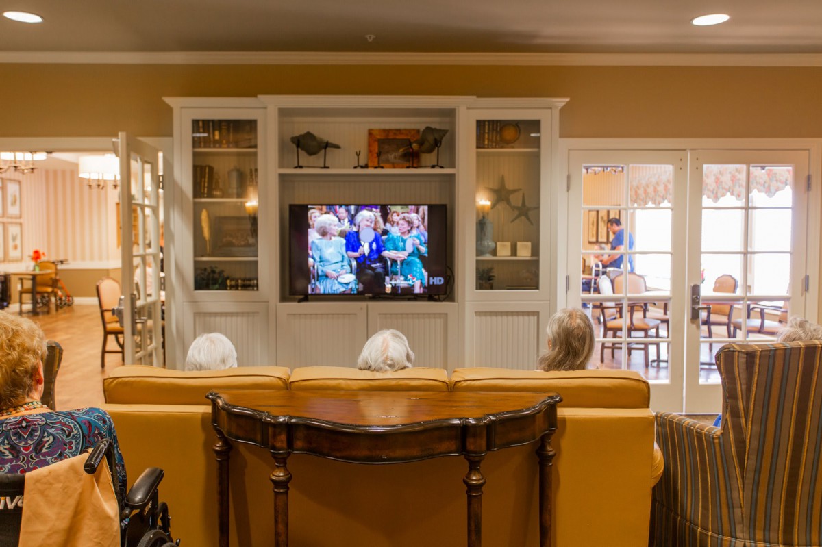 A cozy living room where people are sitting on a sofa, watching television.