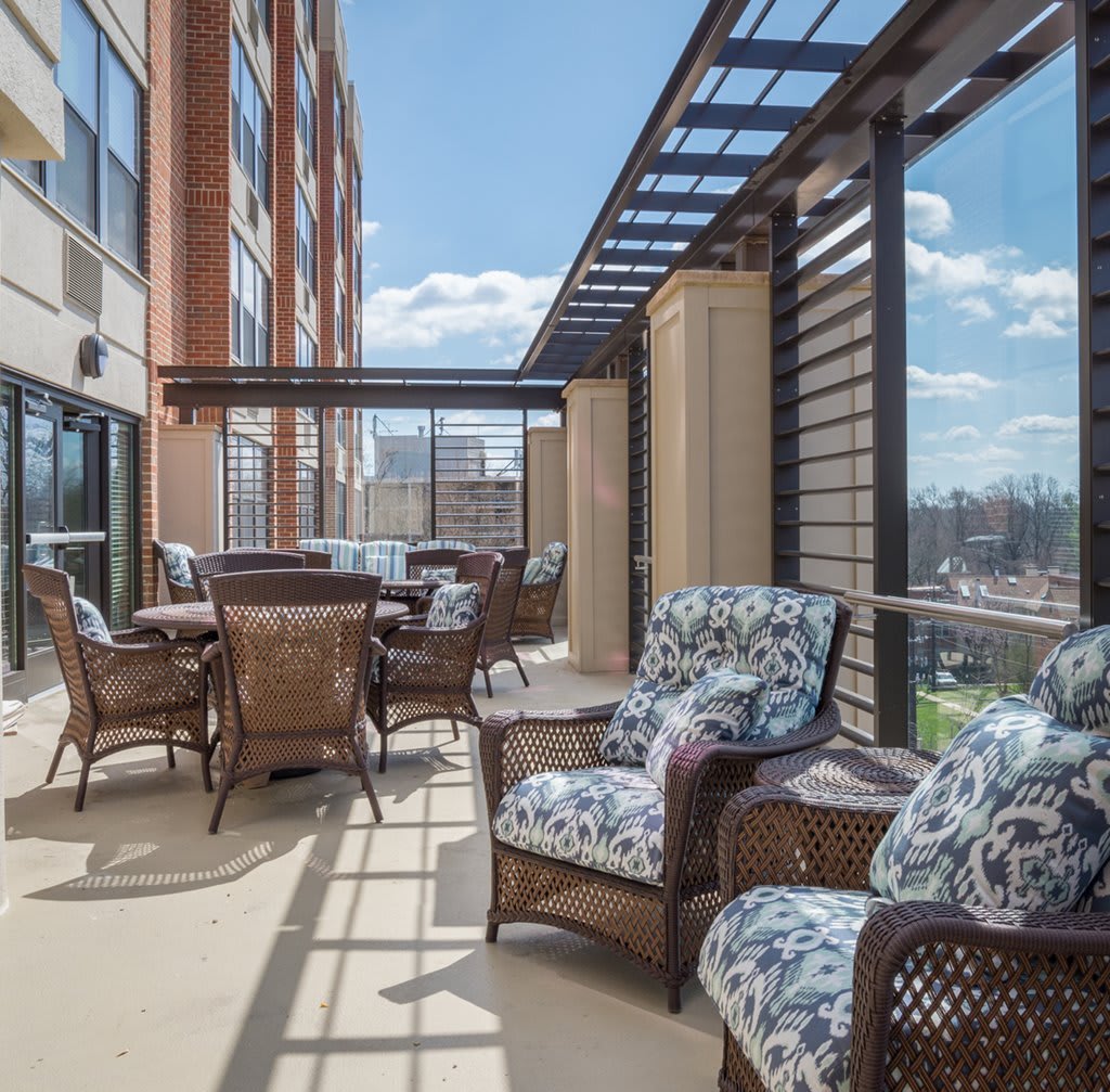 A spacious outdoor balcony with comfortable seating and a table, offering a sunny urban view.