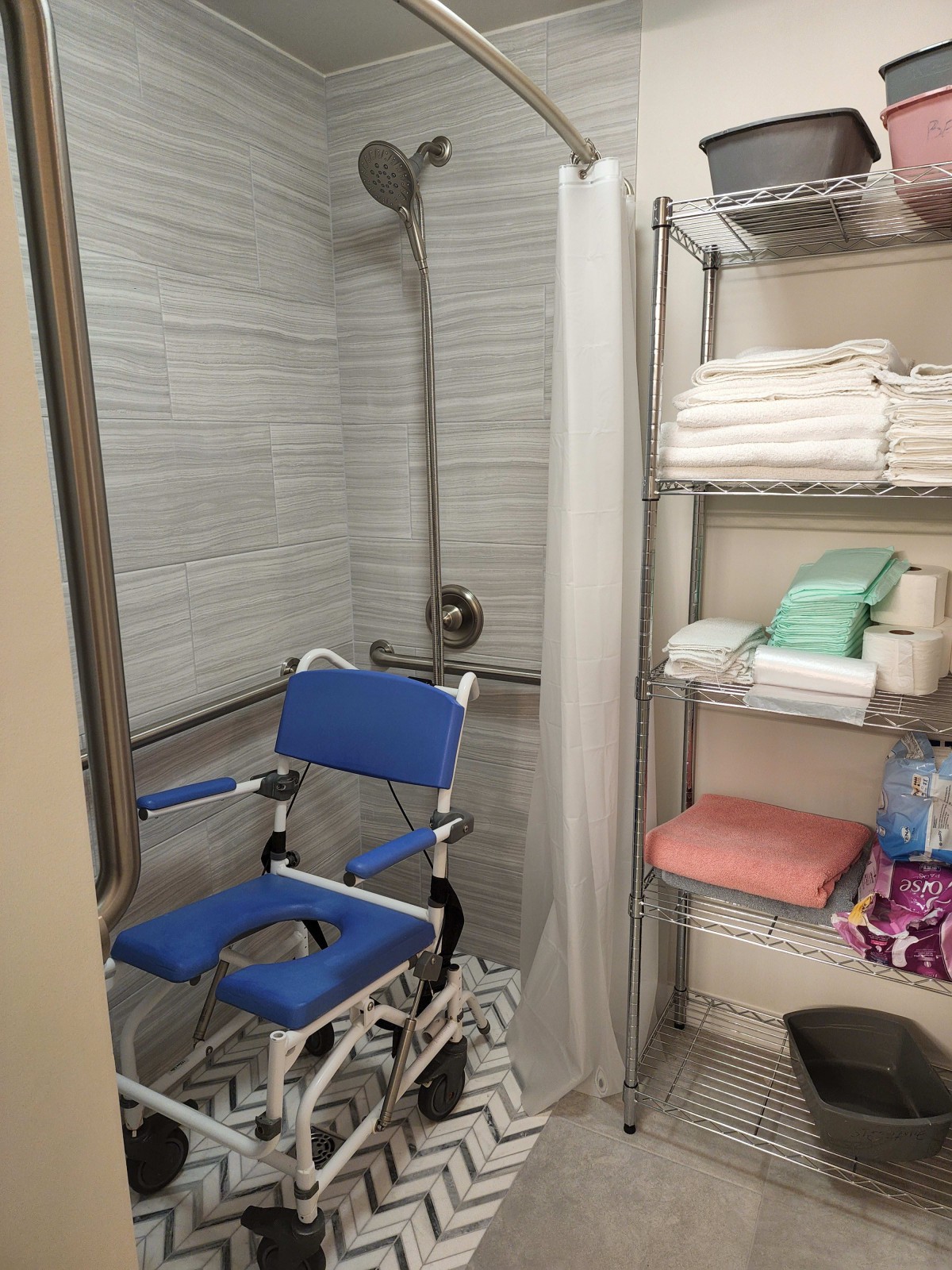 An accessible bathroom with a shower chair and neatly stacked towels on shelves.