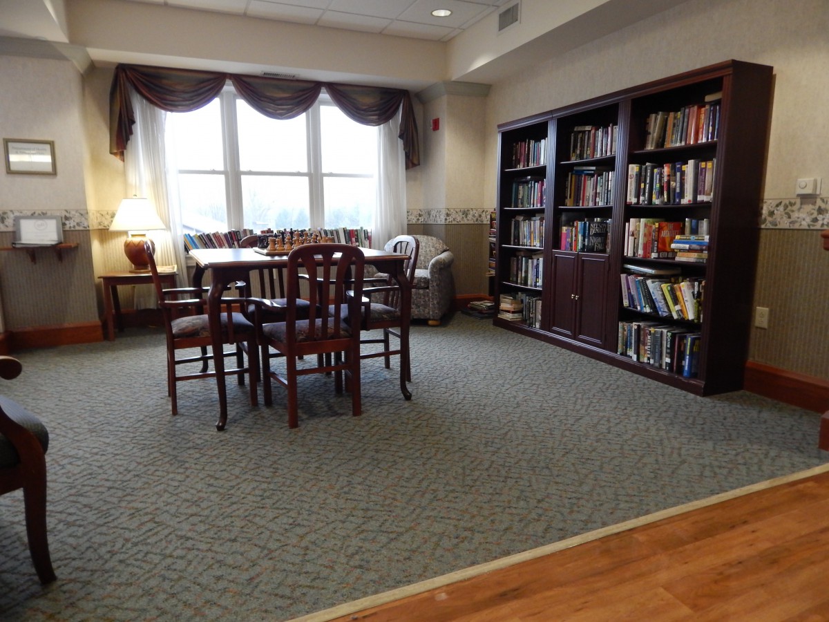 A cozy library space with bookshelves, a table and chairs, and natural light from a large window.