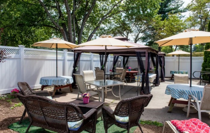 A cozy outdoor patio area with gazebos, umbrellas, and various seating options surrounded by trees.