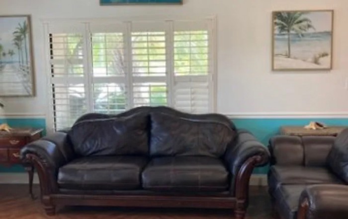 A cozy living room featuring a dark leather sofa and armchair, complemented by wall art and shuttered windows.