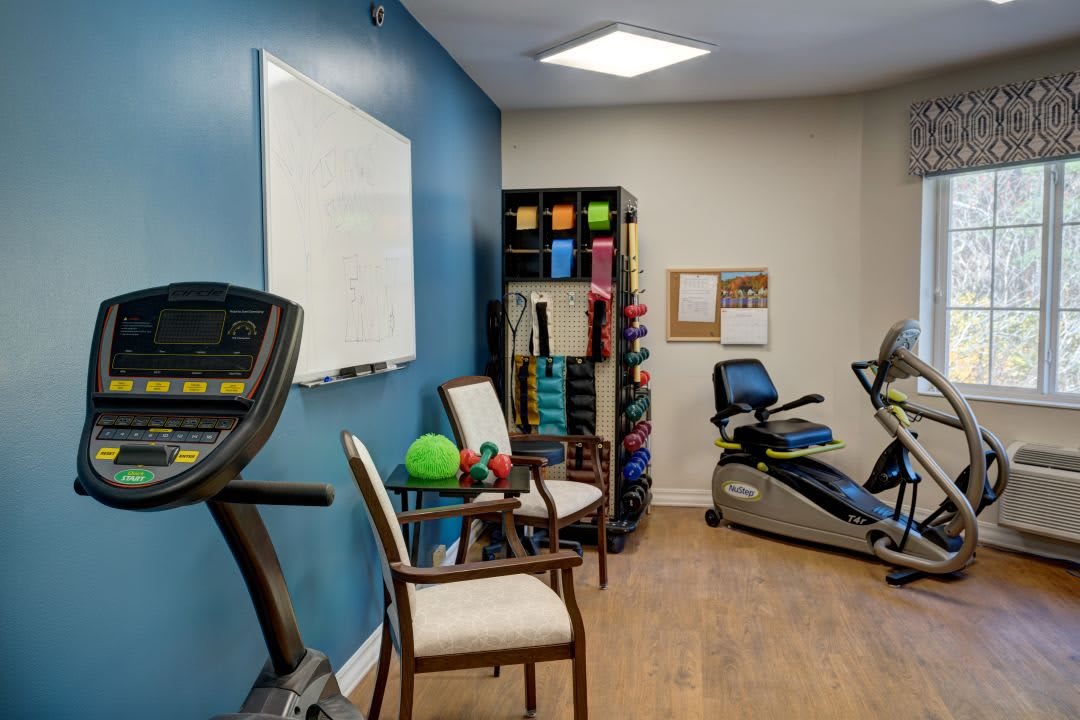 A small exercise room equipped with various fitness machines and gear, including a treadmill, exercise bike, and weights.