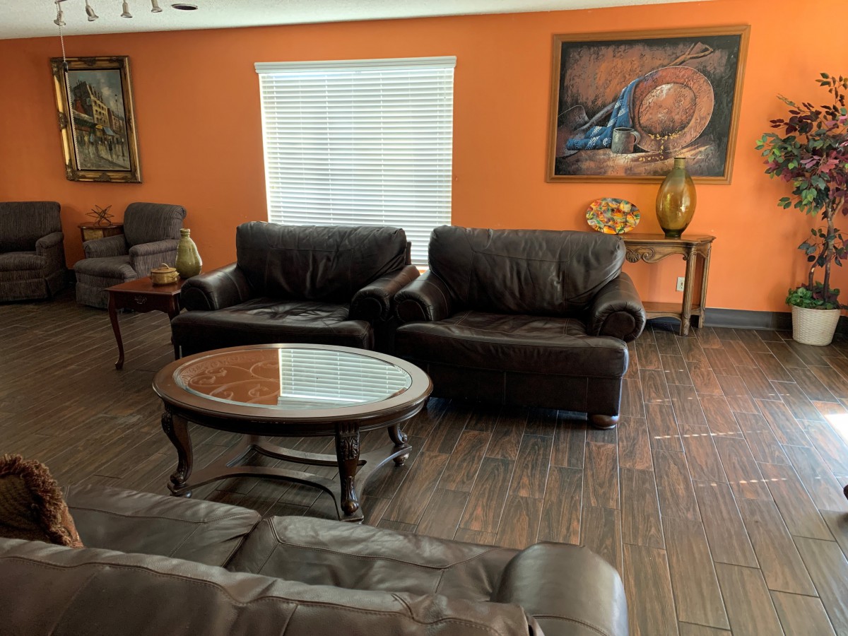A cozy living room with dark sofas, a round coffee table, and colorful artwork on an orange wall.