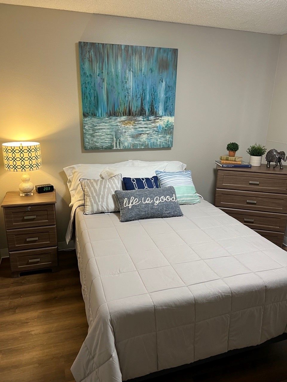 A cozy bedroom with a neatly made bed, illuminated by a bedside lamp and adorned with decorative pillows.