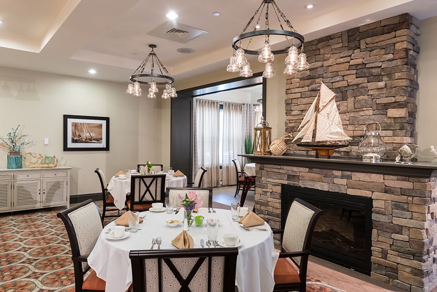 An elegantly set dining room with a stone fireplace and model sailboat decor.