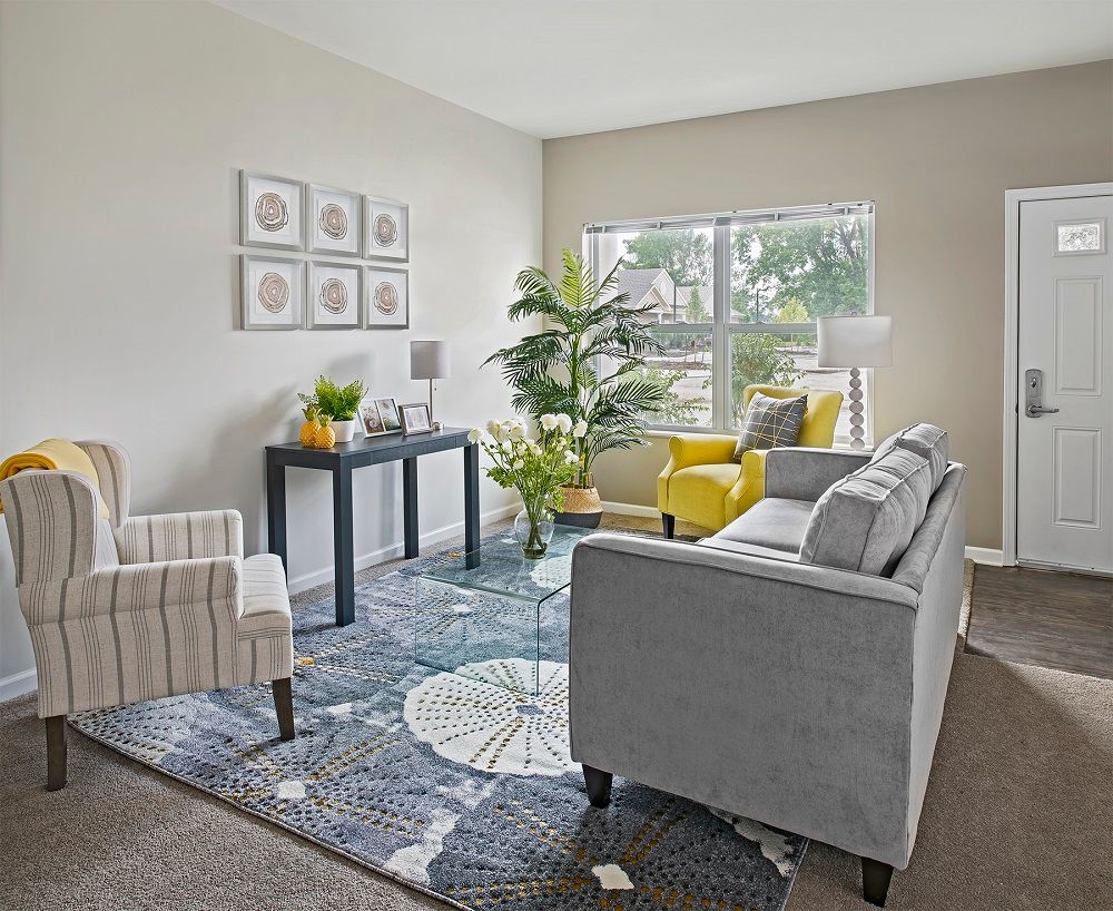 A modern living room with stylish furniture, including a gray sofa, a yellow armchair, and decorative elements such as houseplants and wall art.