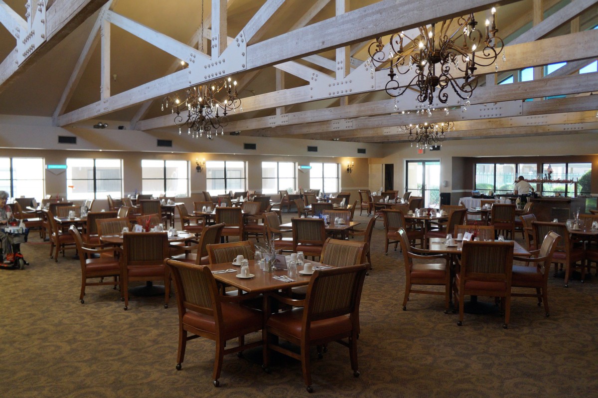 A spacious restaurant dining room with multiple tables and elegant chandeliers.