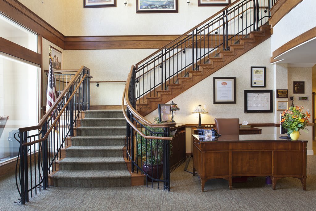 A well-lit office interior with a staircase, wooden desk, and framed artwork on the walls.