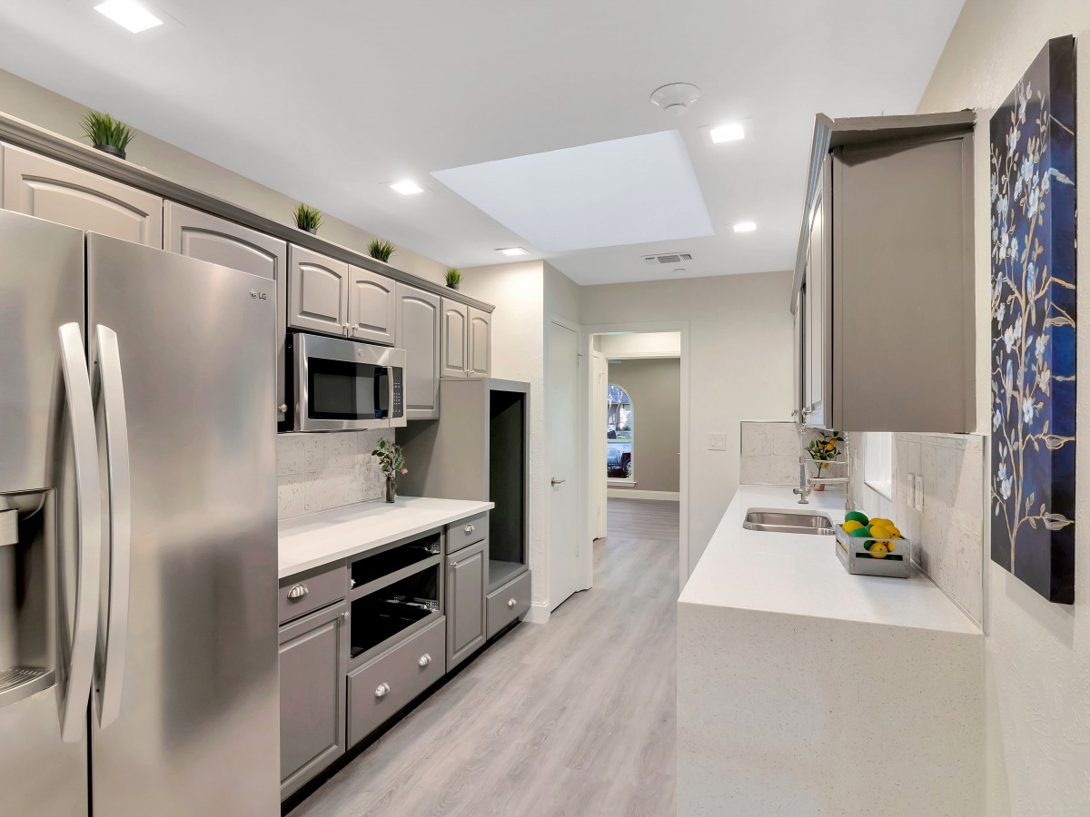 A modern kitchen featuring stainless steel appliances, sleek white countertops, and light wood flooring.