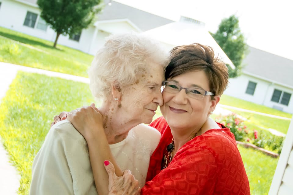 A younger woman embraces an elderly woman outdoors, showing affection and warmth.
