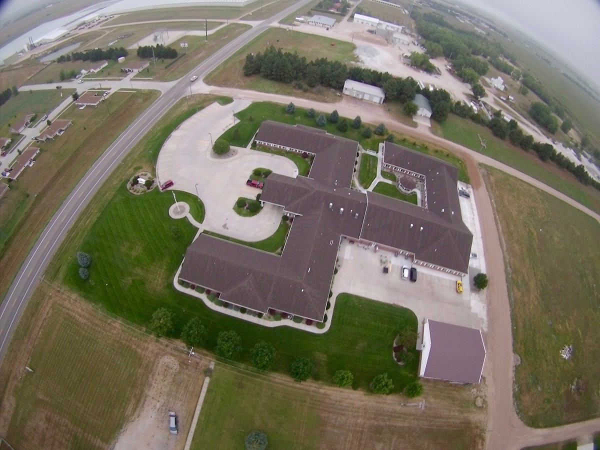 Aerial view of a building complex adjacent to a road, surrounded by greenery.