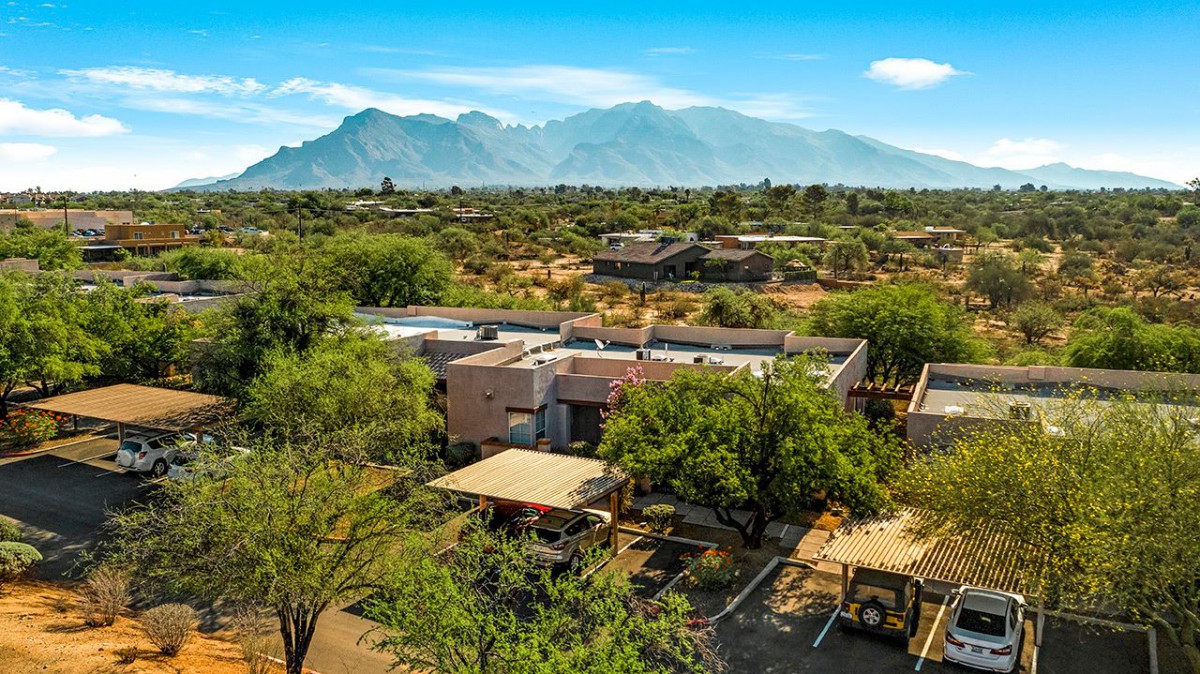 A scenic view of a desert landscape with mountains in the background and a house surrounded by trees.