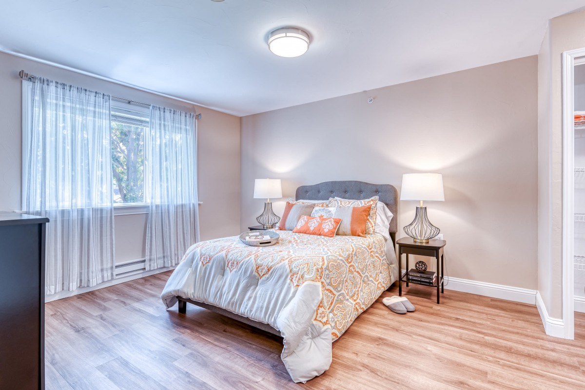 A modern bedroom with a cozy and minimalist design, featuring a comfortable bed, two lamps, and wooden flooring.