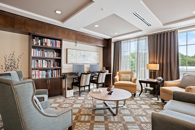 A modern library room featuring bookshelves, computers, seating area, and large windows.