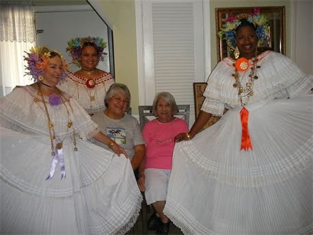 A group of women wearing traditional dresses and colorful accessories pose together for a photo.
