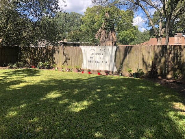 A backyard with a fence displaying a large sign on a sunny day.