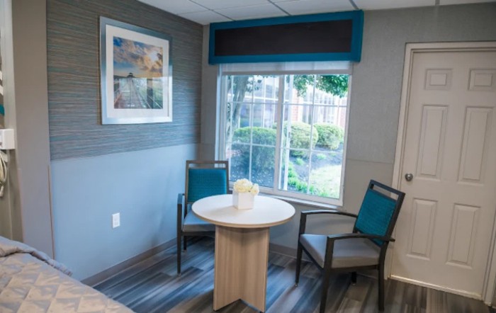 A modern waiting room with a small table, two chairs, and a window overlooking greenery.