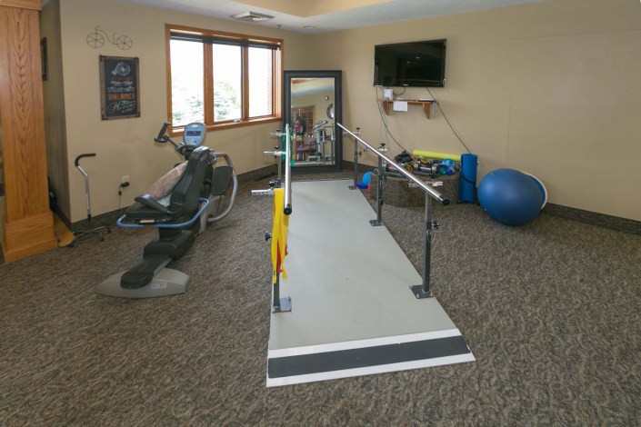 A physical therapy room equipped with rehabilitation tools including parallel bars, exercise machines, and a therapy ball.