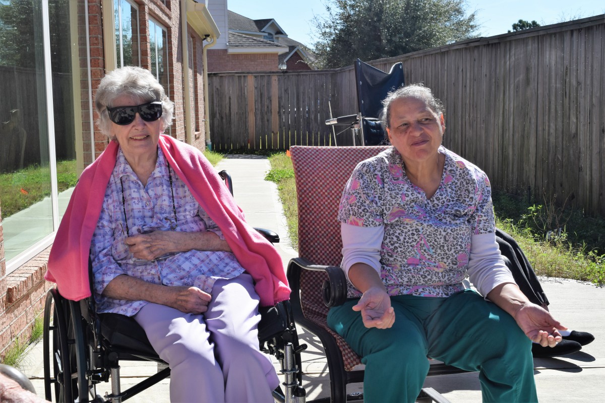 Two elderly women enjoying a sunny day outdoors, one seated in a wheelchair and the other beside her.