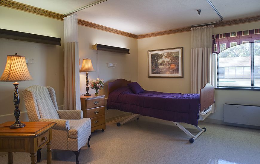 A well-furnished hospital room featuring a bed, comfortable seating, and warm lighting.