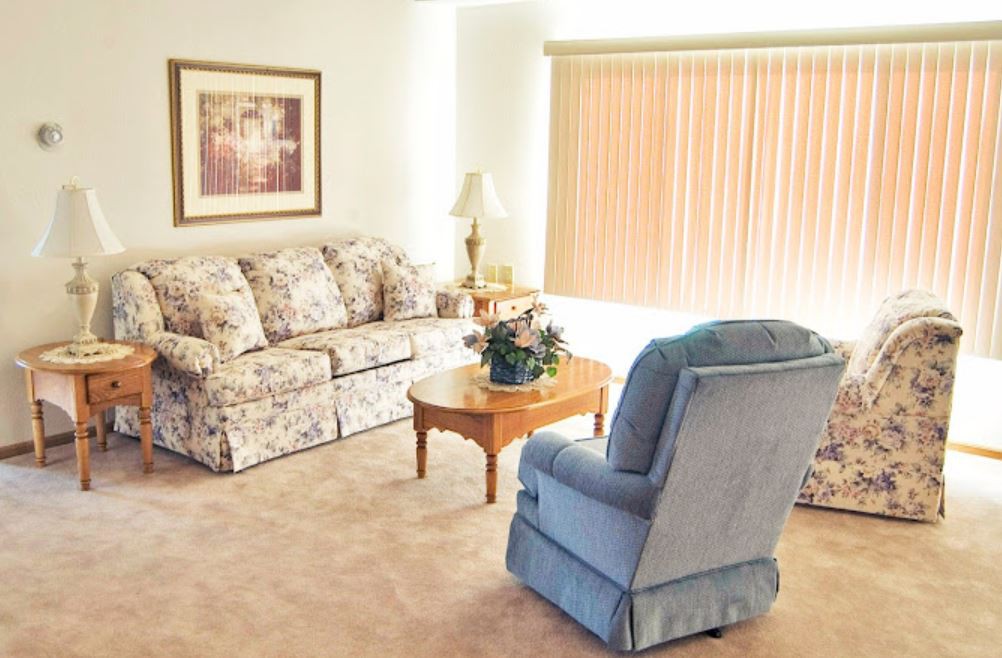 A cozy living room with a floral sofa, blue armchair, and wooden coffee table.