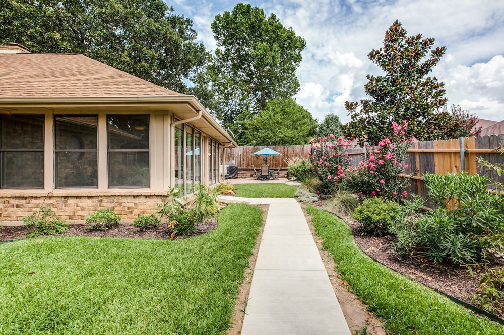 A beautiful backyard with a concrete pathway surrounded by lush greenery and blooming flowers.