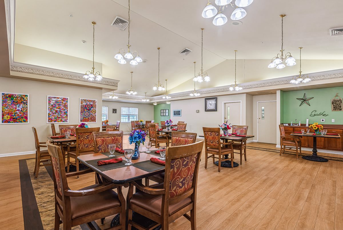 A spacious and elegantly decorated dining room with multiple tables and chairs, featuring modern chandeliers and wooden flooring.