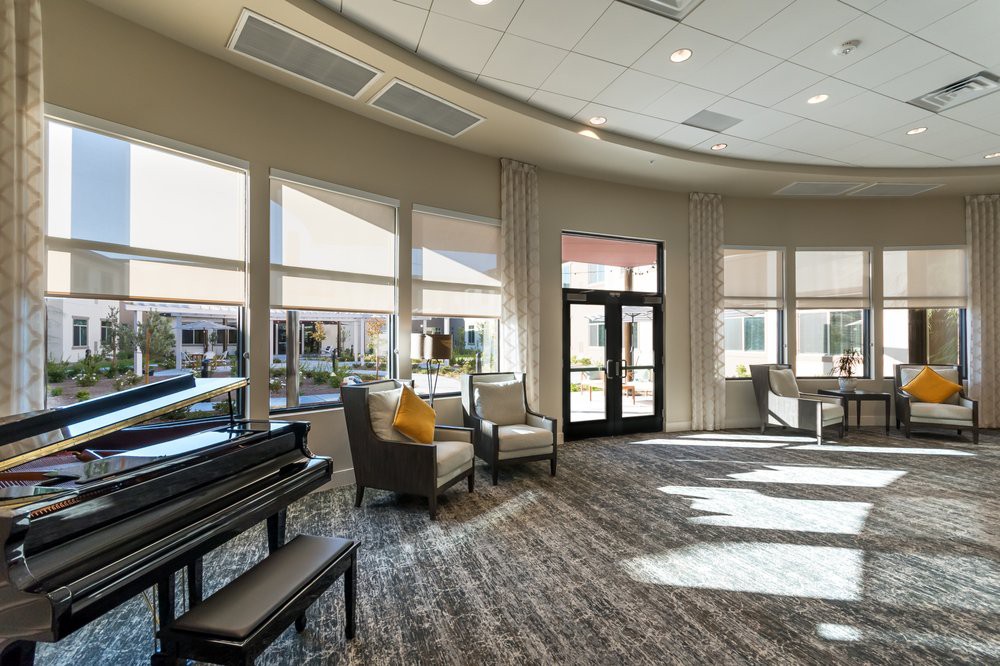 A well-lit interior with a piano and comfortable seating area surrounded by large windows.