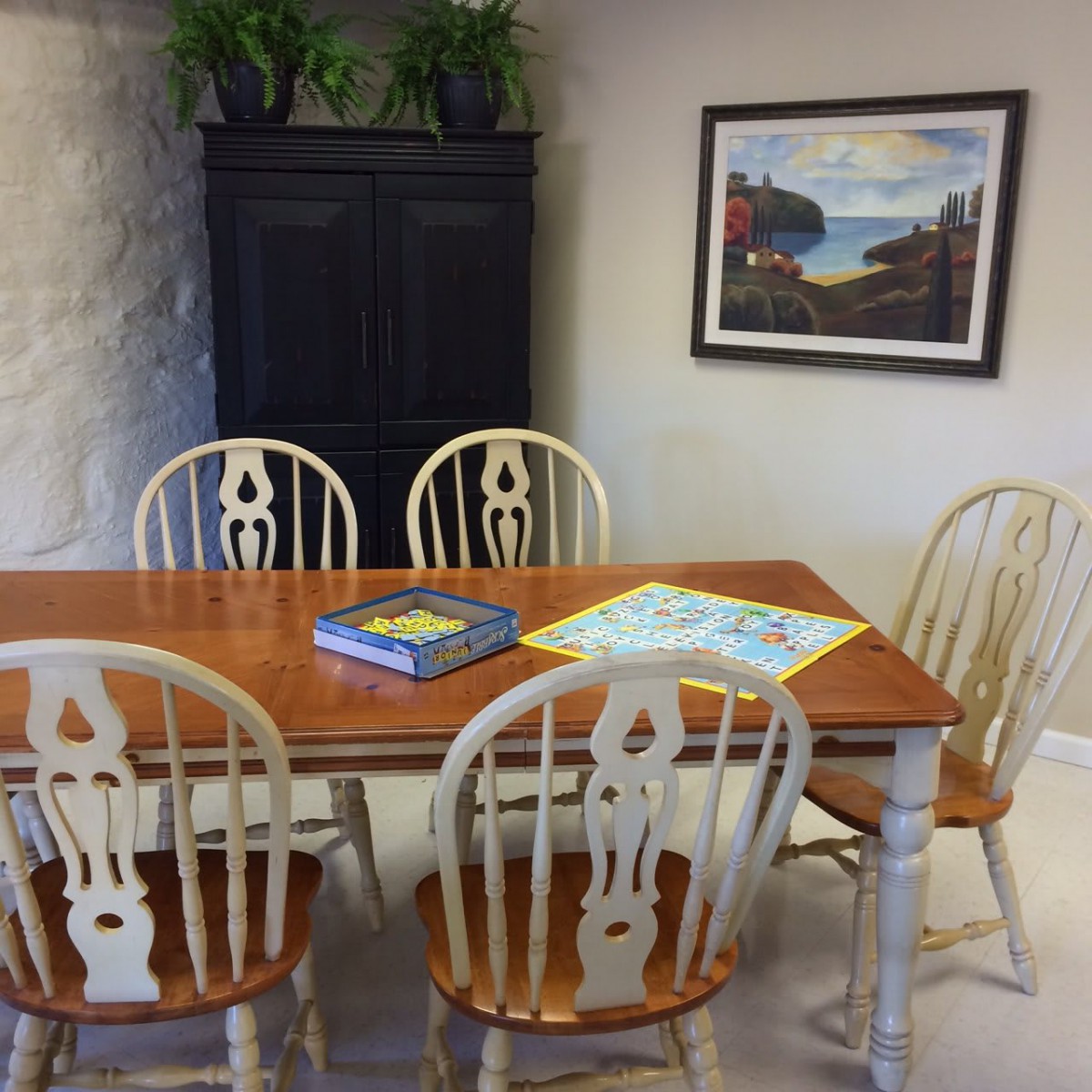 A cozy dining area with a wooden table and chairs, decorated with artwork and plants.