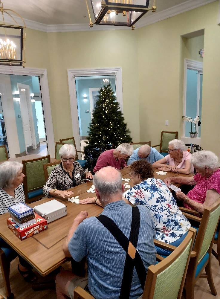 A group of seniors playing cards around a table in a room with a Christmas tree.