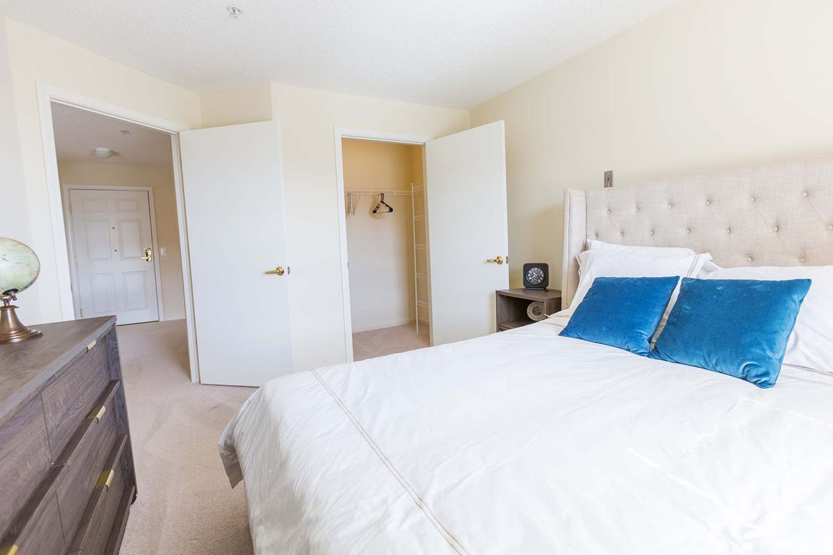 A bright and minimalist bedroom with a neatly made bed, white walls, and an open closet door.