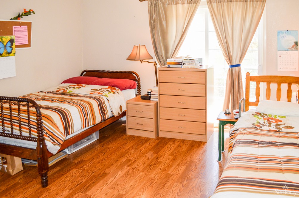 A cozy bedroom with two single beds, a small lamp, and wooden furniture on a wooden floor.