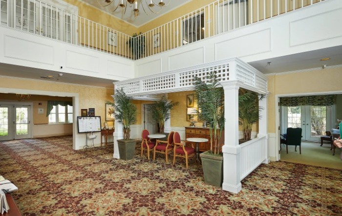 A hotel lobby with decorative plants, seating area, and a balcony overlooking the space.