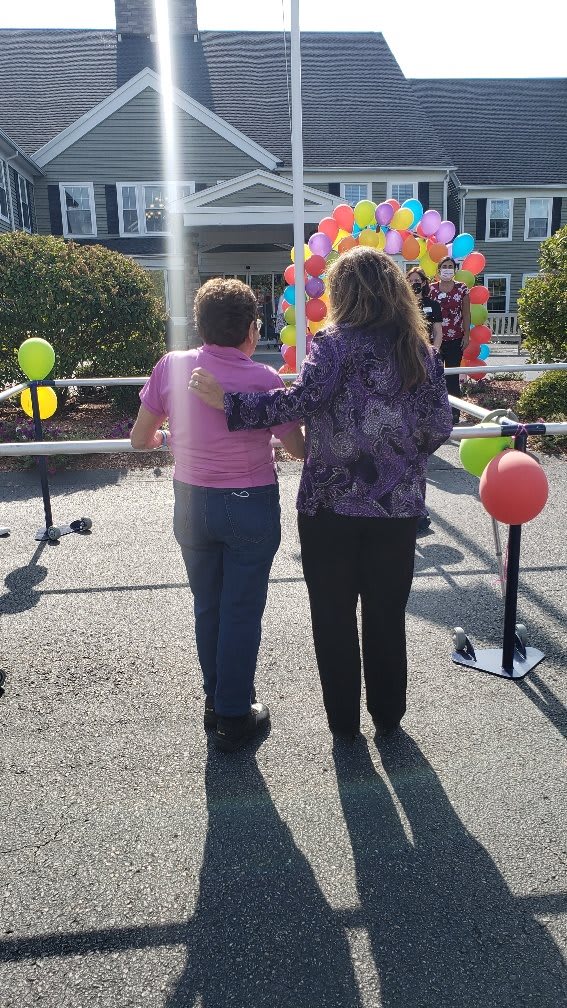 Two people walking towards a colorful balloon display, arm in arm, during an outdoor event.