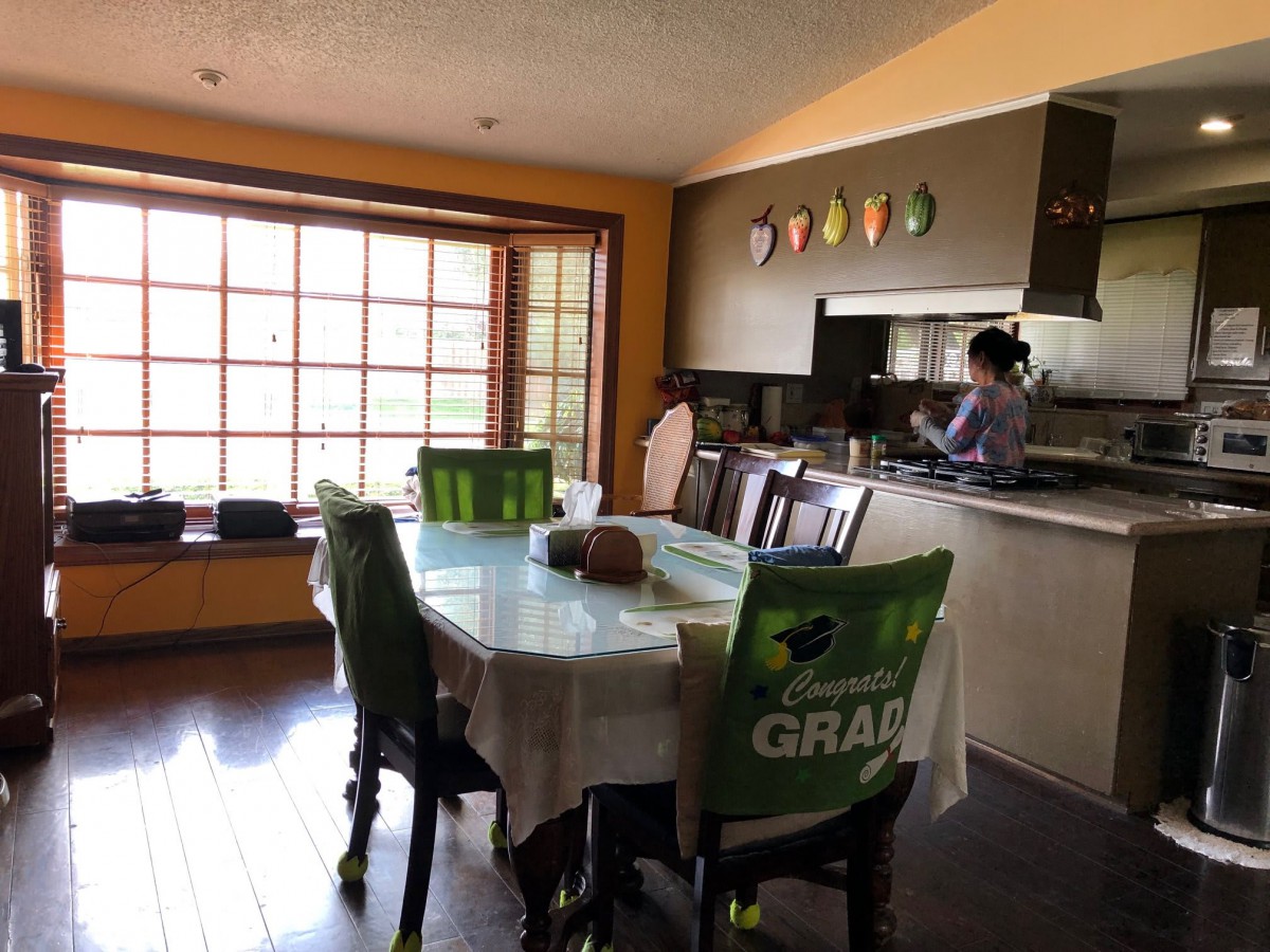 A cozy dining area with a table and chairs, adjacent to the kitchen where someone is preparing food.