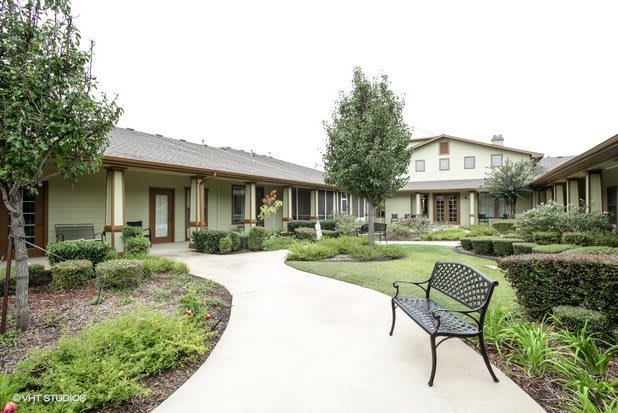 A peaceful garden with a paved pathway, surrounded by buildings and greenery.