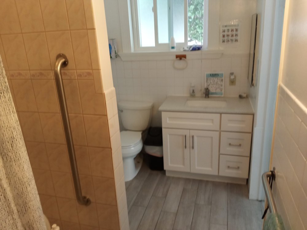 A modern bathroom with a toilet, sink, and vanity, featuring a grab bar next to the shower area.