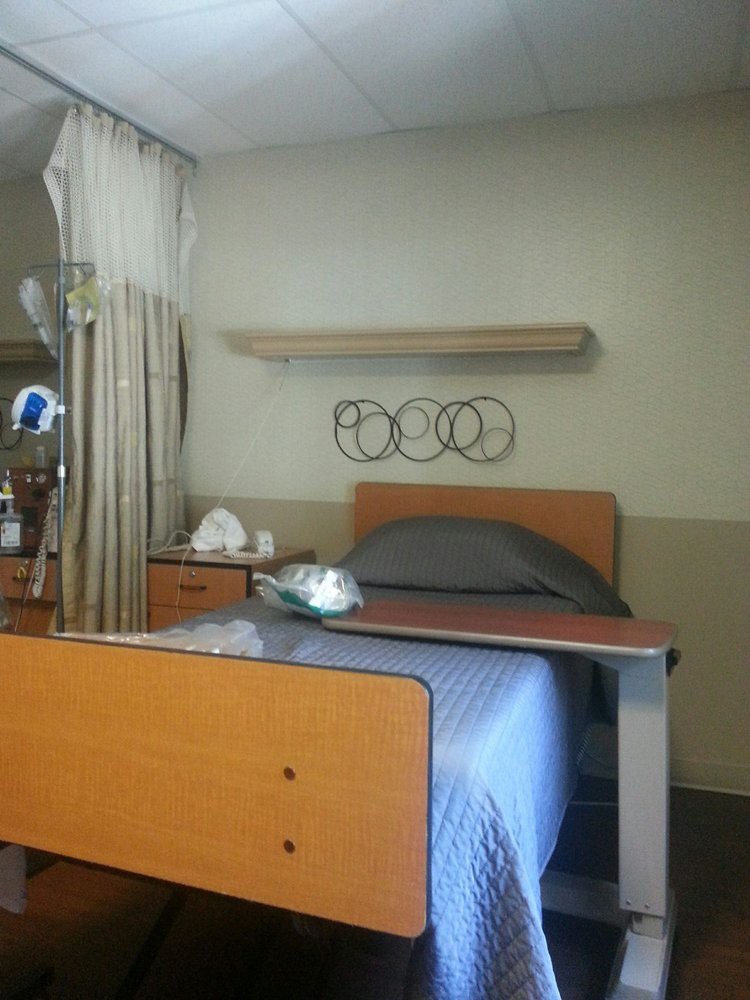 A hospital room with a bed, bedside table, and curtains.