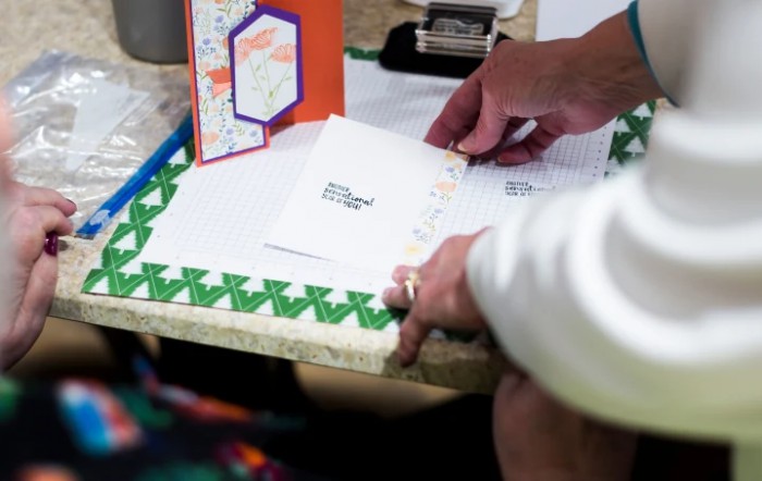 A person writing on envelopes with greeting cards nearby on a table.